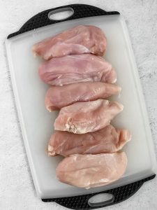A cutting board has raw chicken breasts on it to prep for the best grilled chicken.