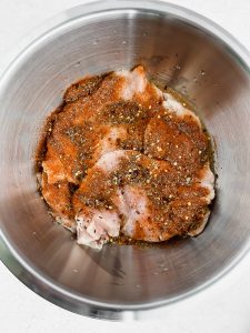A stainless steel bowl is filled with raw chicken breasts sitting in a lime juice marinade.