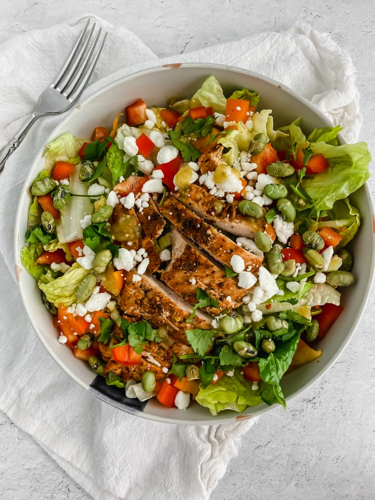 A fresh green salad is topped with sliced pieces of the best grilled chicken. There's a white linen and fork to the side.