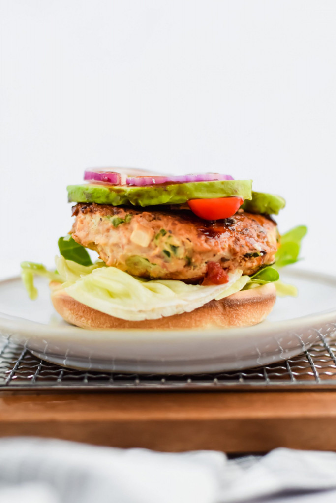 one roasted garlic chicken burger, open faced and topped with tomato, avocado, and red onion on white plate