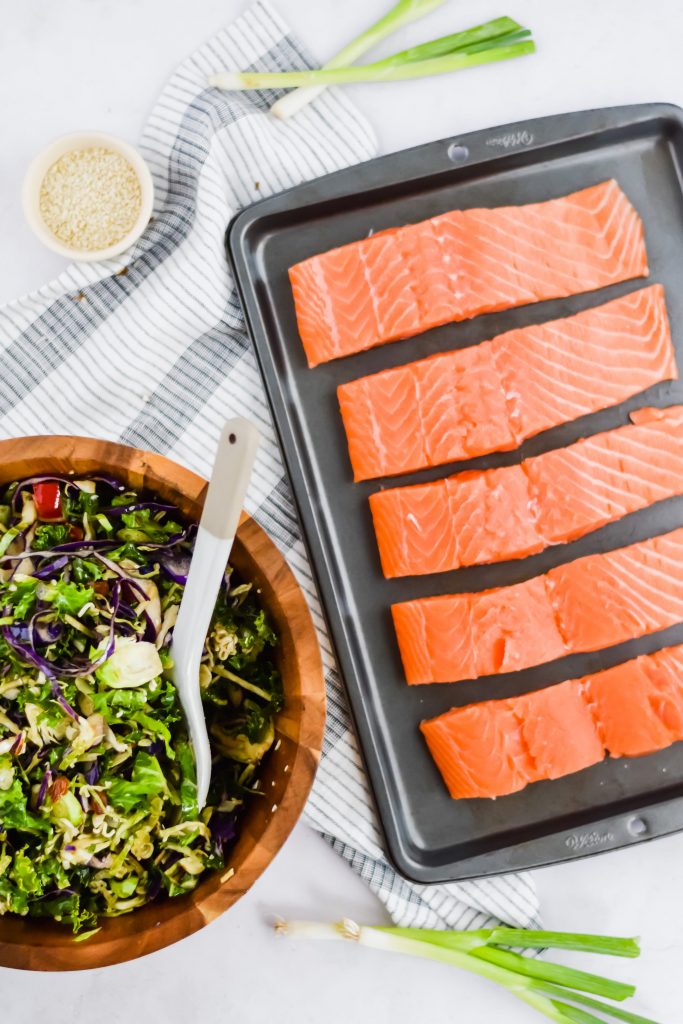 five pieces of raw salmon sliced on baking sheet with chopped salad on the side