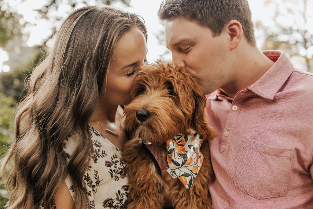 couple holding a puppy kissing her head at the same time