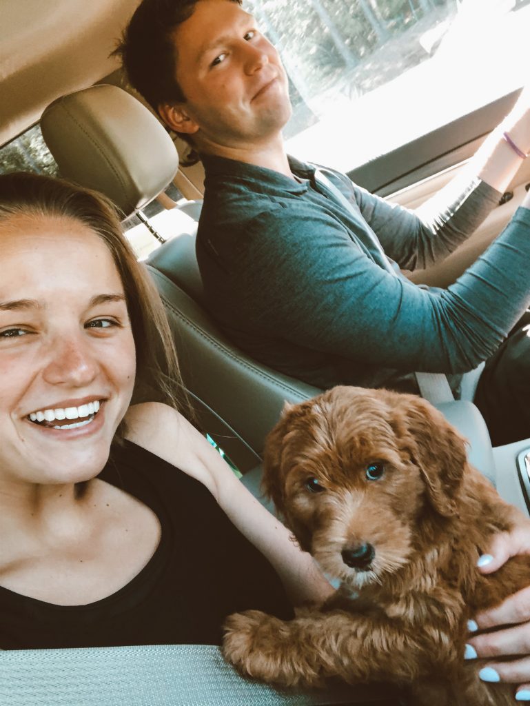 family selfie with girl smiling and holding puppy and guy driving