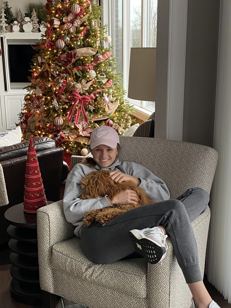 girl in cozy outfit snuggling with shaggy dog in a chair during the holidays