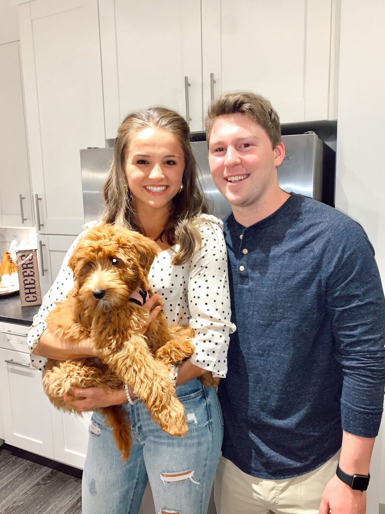 couple holding small puppy in all white kitchen