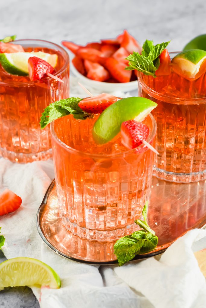 overhead view of Caribbean rum punch garnished with fresh strawberries and lime on silver tray with bowl of strawberries in background