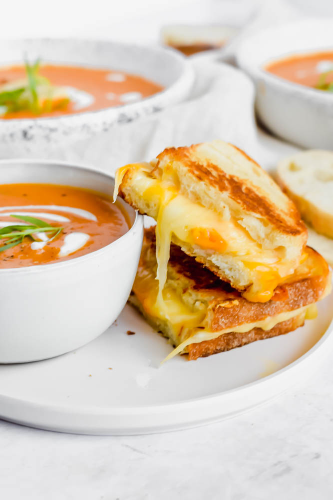 bowl of tomato soup with two pieces of grilled cheese aside it with cheese pull