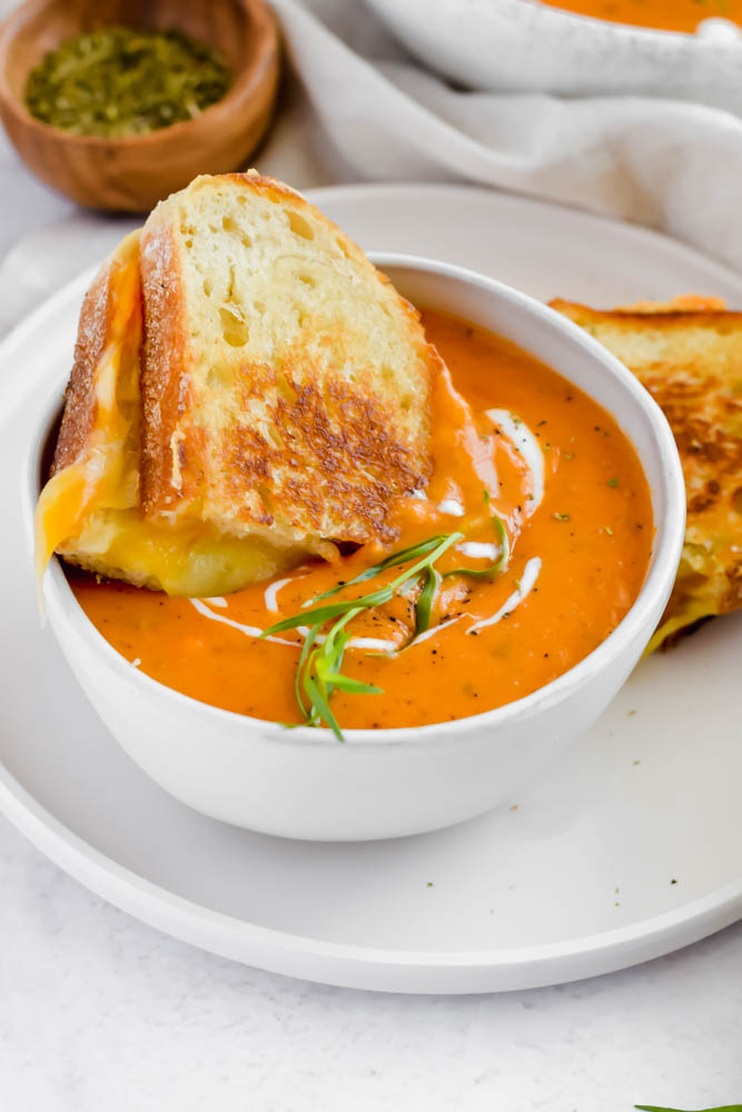 piece of grilled cheese being dunked into a big bowl of roasted tomato soup