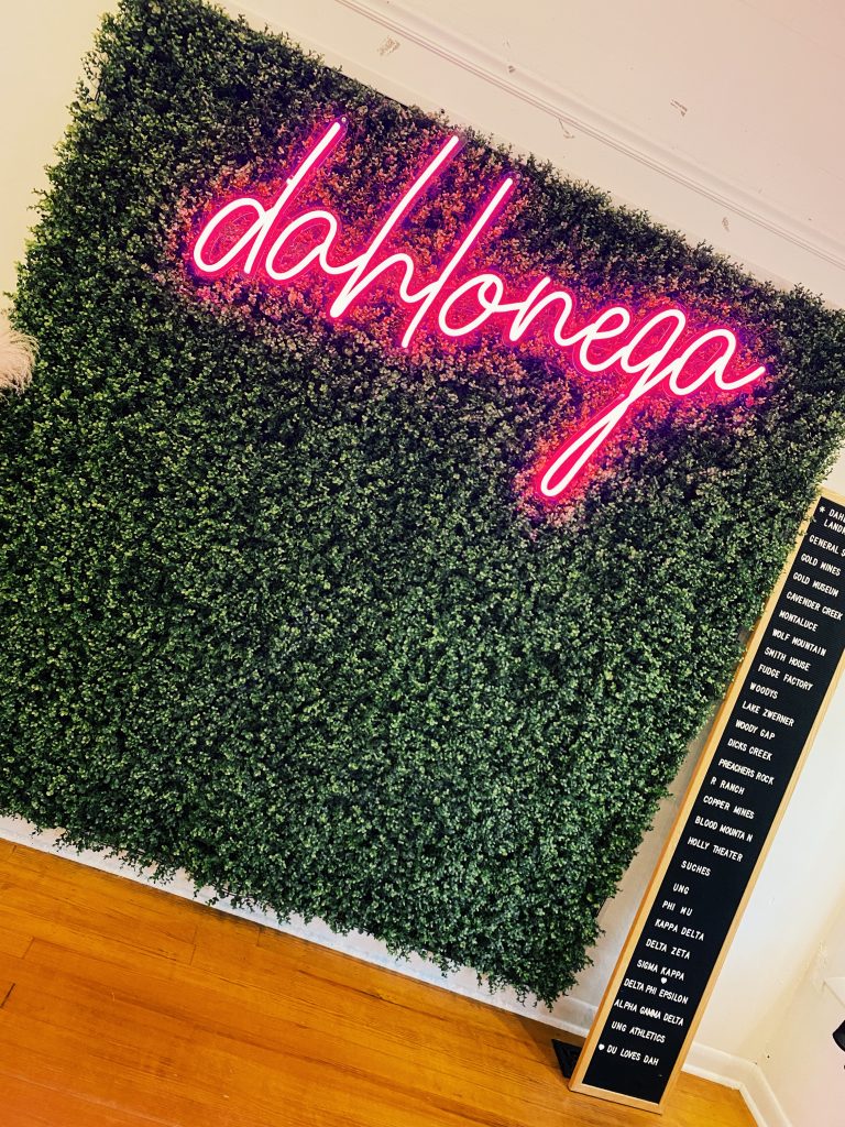 green wall backdrop with neon lit sign that says Dahlonega