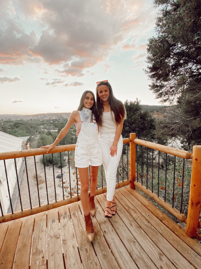 two girls standing on a deck overlooking the sunset