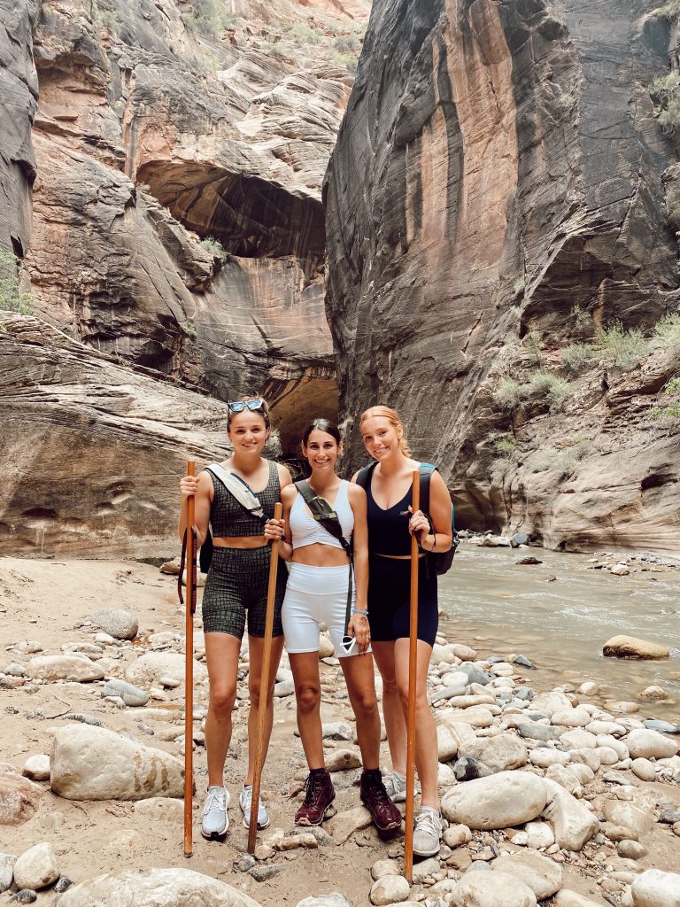 three girls with hiking sticks in the middle of the Narrows in Zion National Park