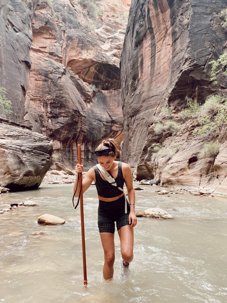 Girl smiling in water hiking with large stick in the middle of the Narrows