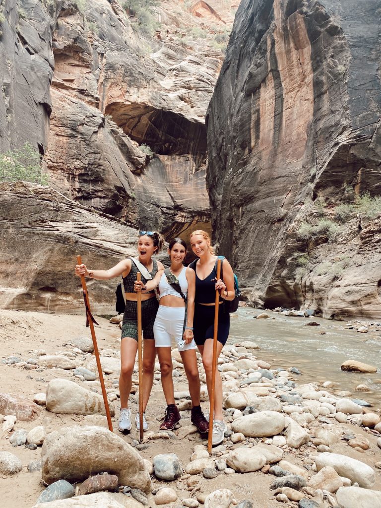 three girls with hiking sticks in the middle of the Narrows in Zion National Park