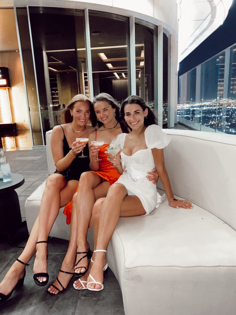 three girls holding drinks sitting on white booth with skyline in the background