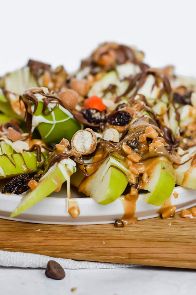 plate of green apples spread in layers topped with melted white chocolate, melted chocolate, m&ms and trail mix