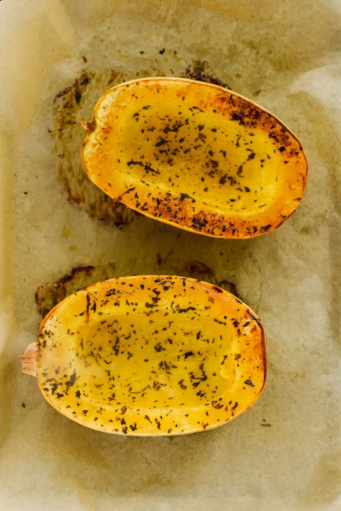 halved baked spaghetti squash sprinkled with herbs on parchment paper