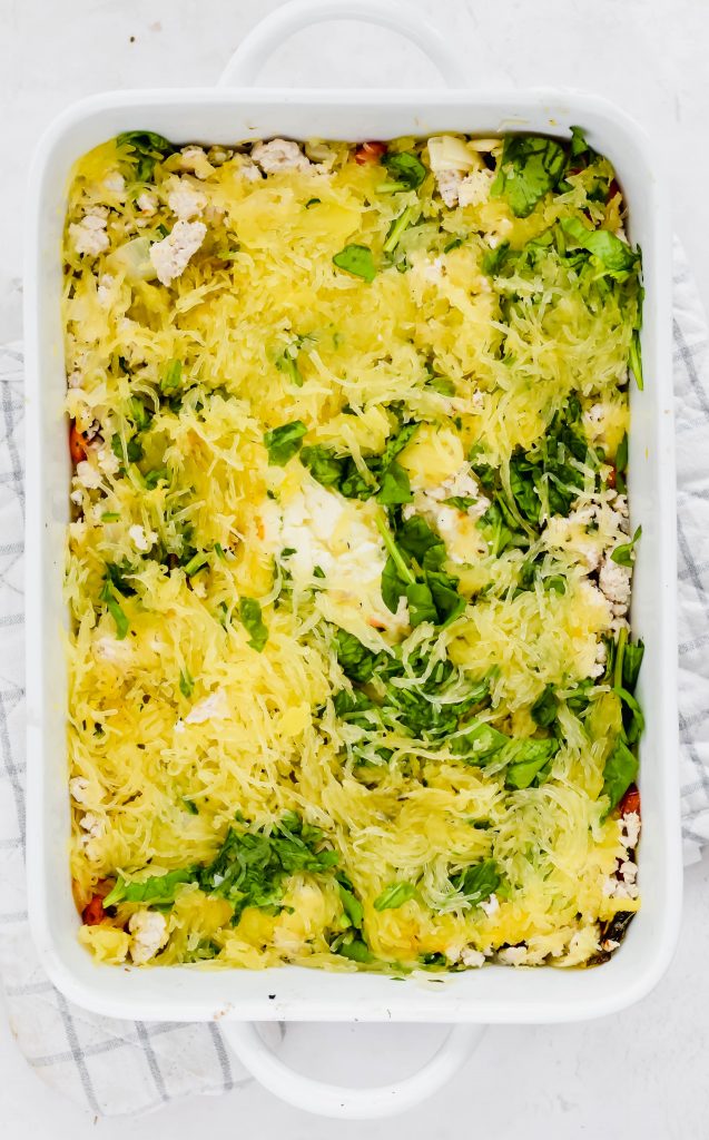 Large white baking dish filled with spaghetti squash during assembly process on white and gray oven mit