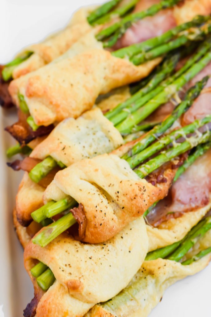angled close up shot of cooked asparagus and bacon pastry on white plate