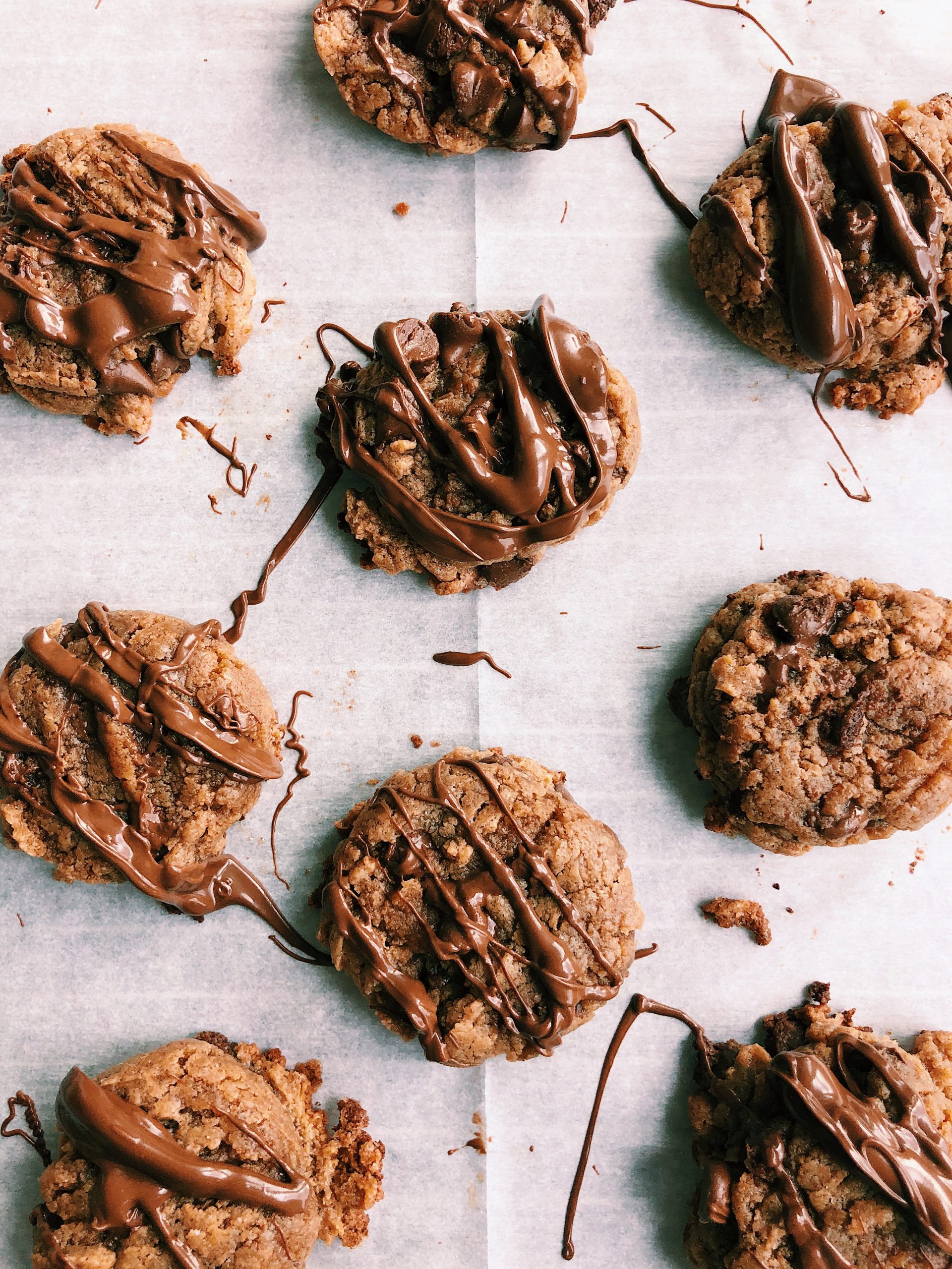 small almond butter blossom cookies drizzled in chocolate on parchment paper.