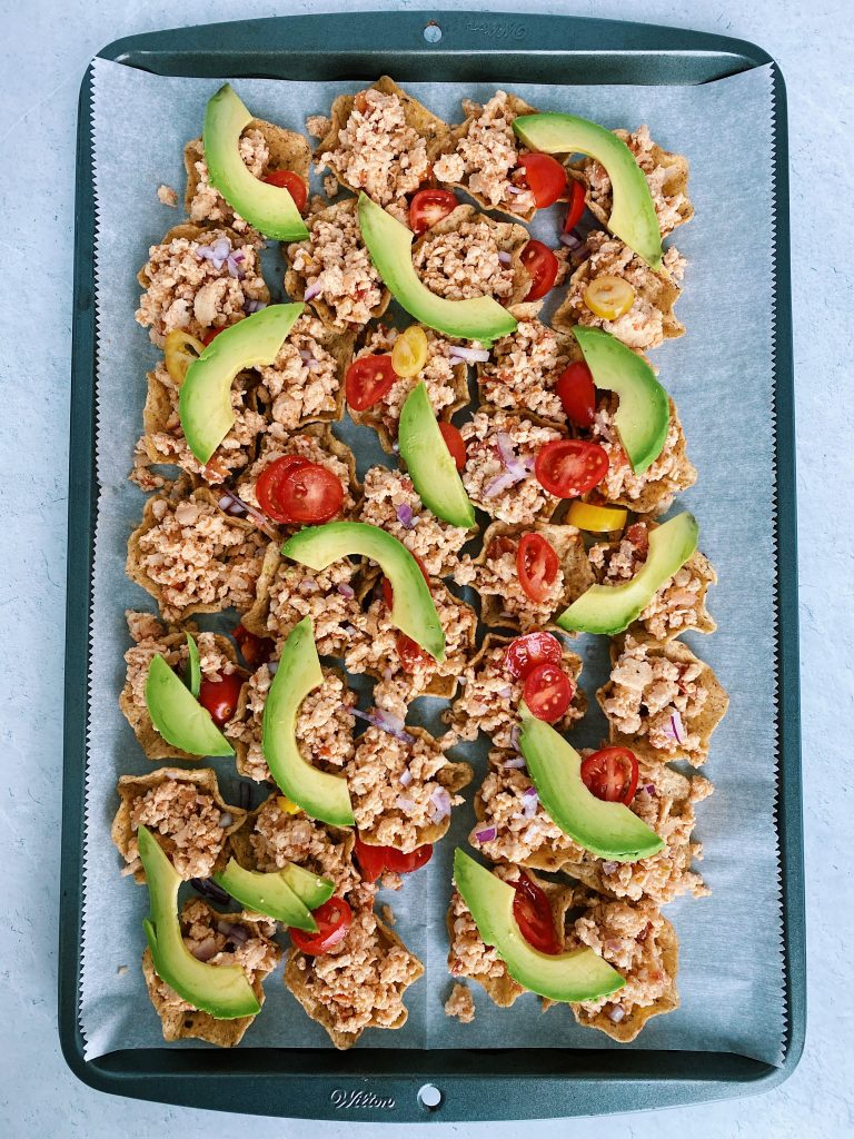 Flat lay image of sheet pan nachos with fresh toppings: avocado and tomatoes