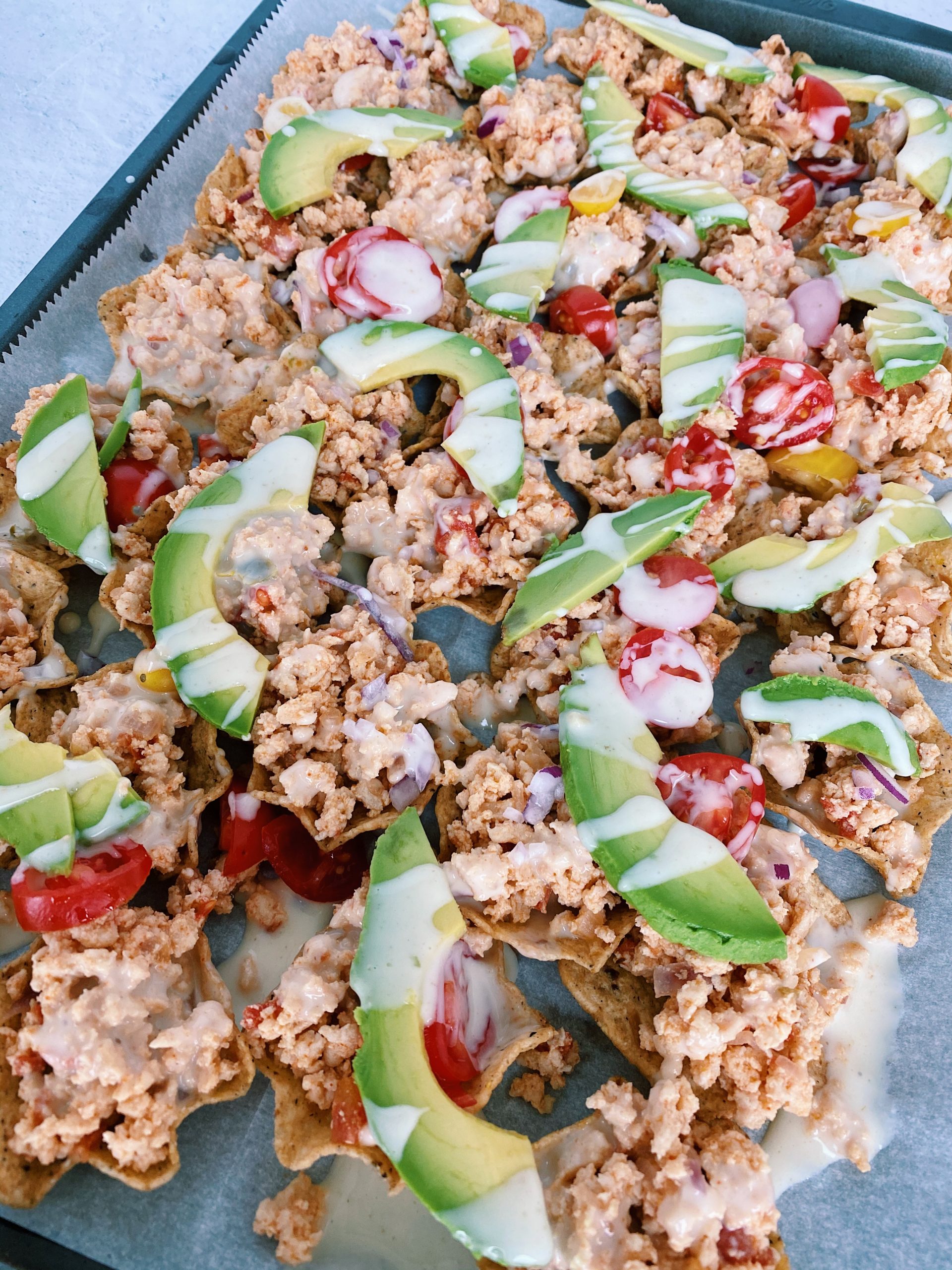 sheet pan game day nachos with drizzled queso and topped with avocado slices.