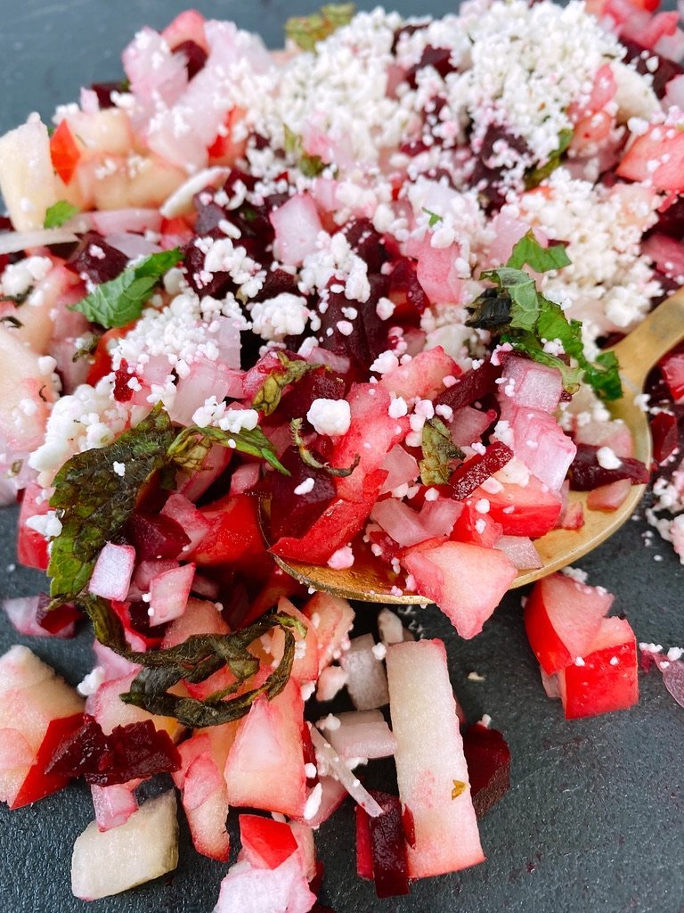 close up image of chopped slaw with lots of crumbled cheese, gold spoon, and black backgroujd