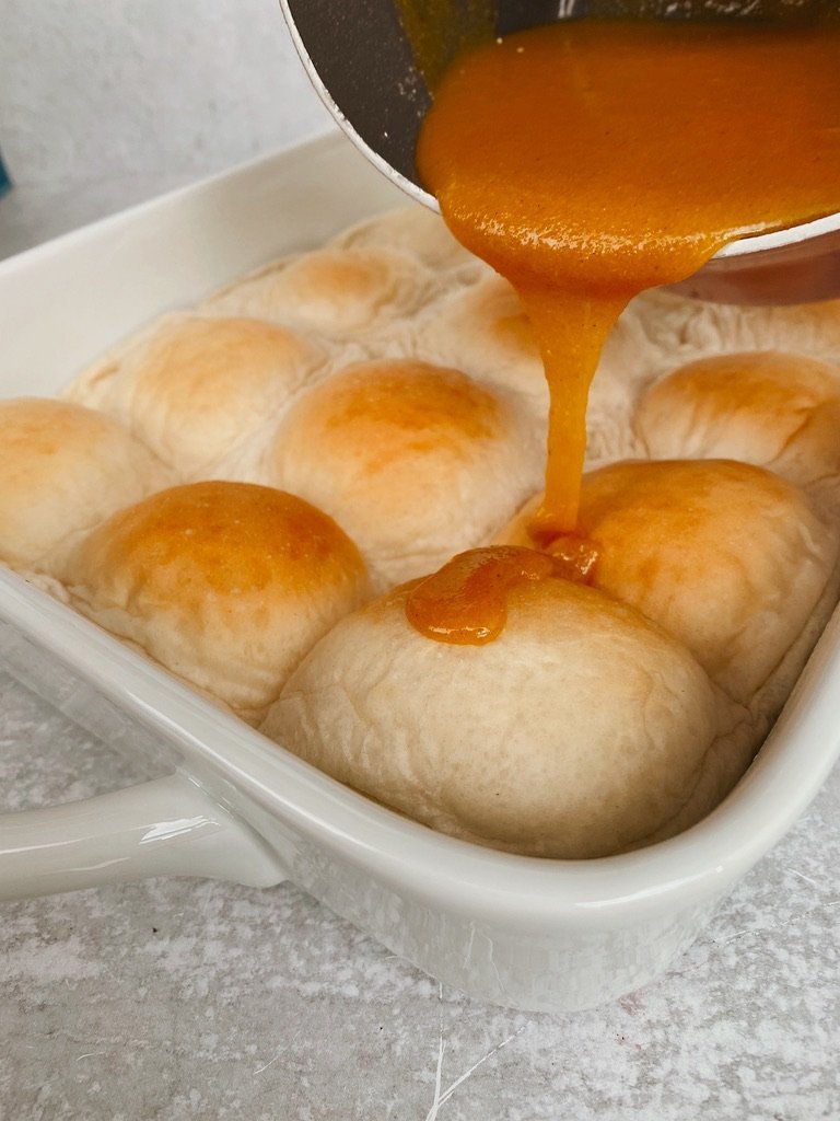 close up image of sauce pan pouring caramel drizzle on toasted buns