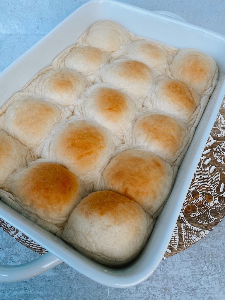 white baking dish with 15 slightly toasted risen buns and concrete backdrop