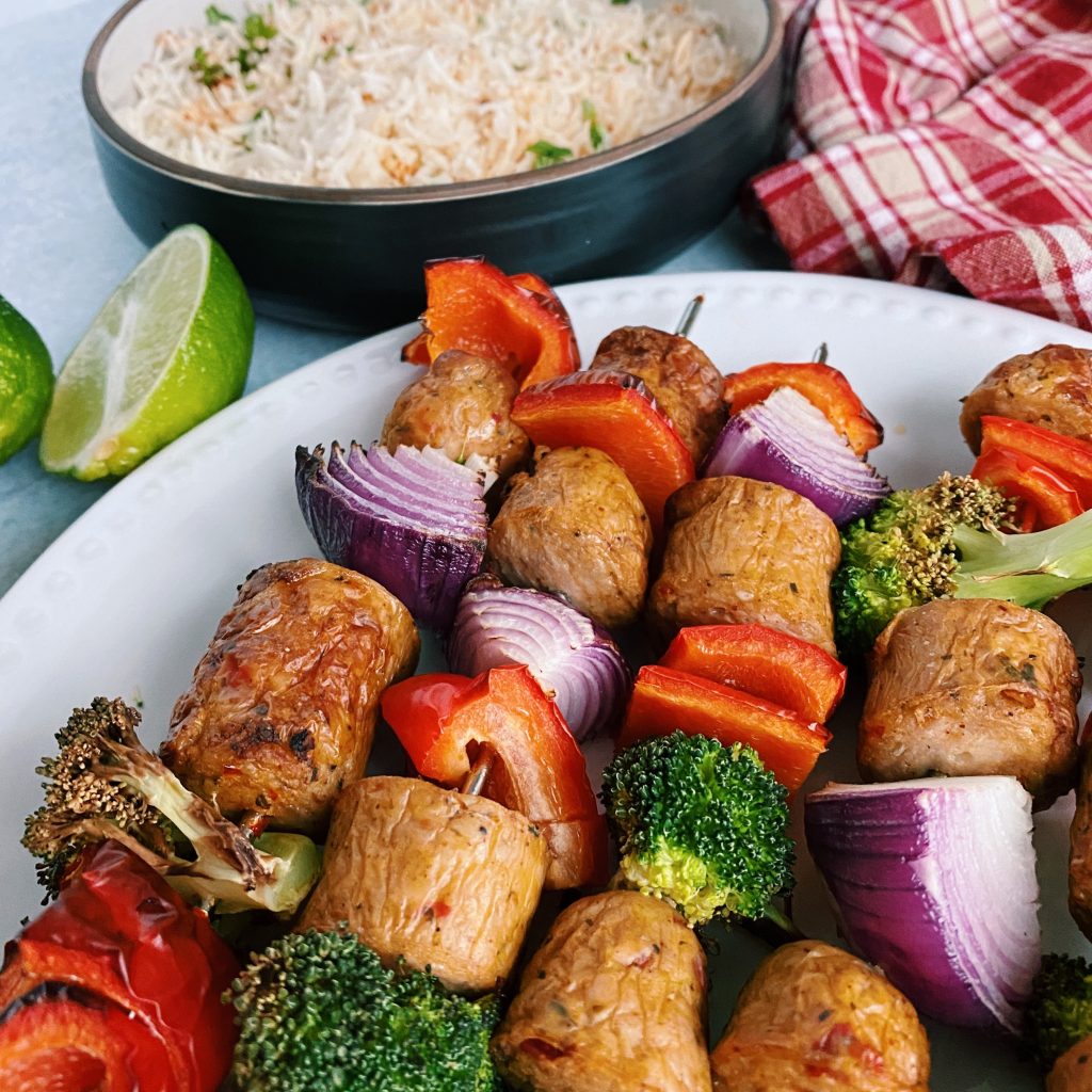 grilled vegetable and sausage kabobs with cooked rice in the background on white plate