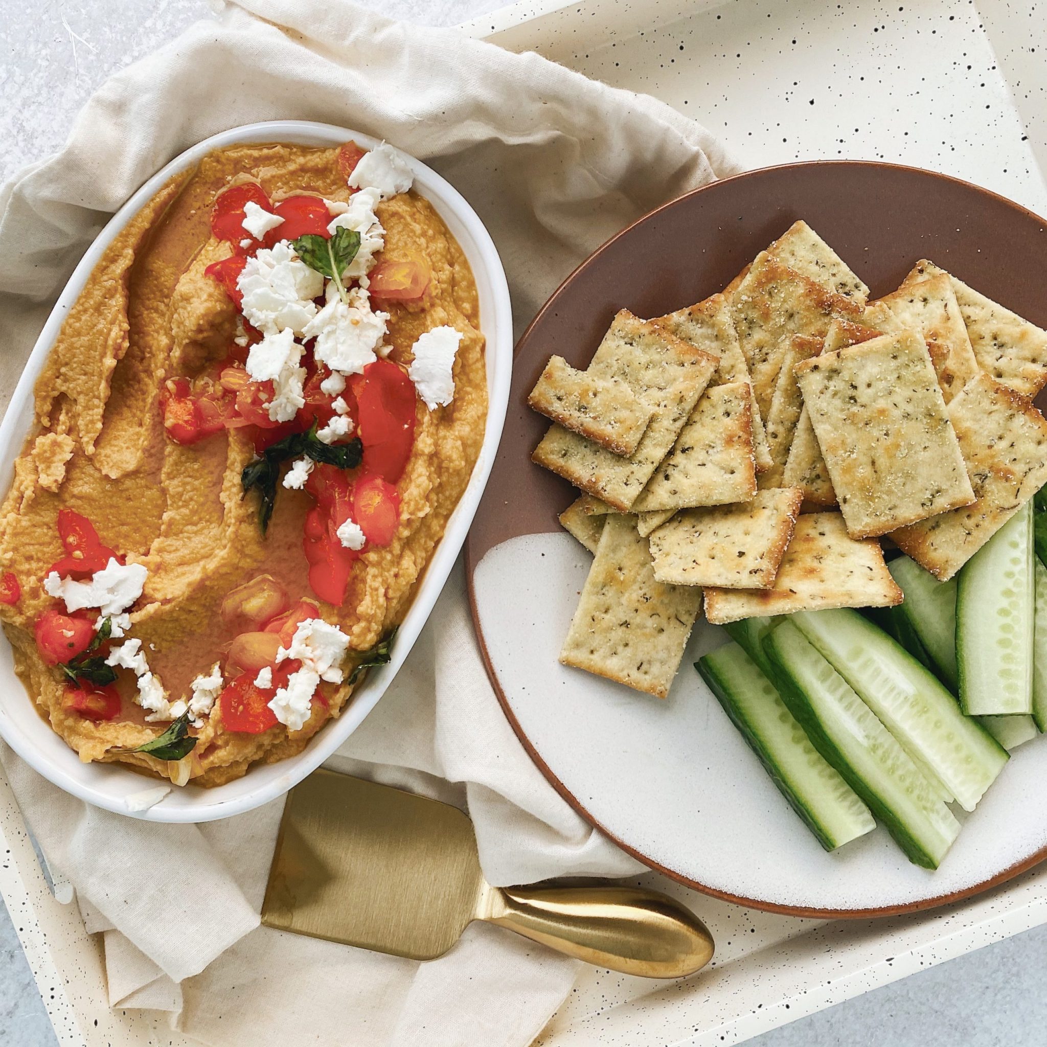 flat lay presentation image of assembled hummus, crackers, and veggies on white speckled tray