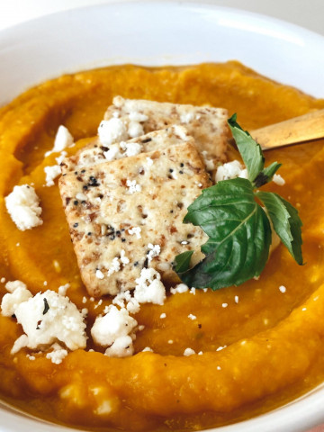 close up image of butternut squash with basil leaf garnish, feta crumbles, and crackers
