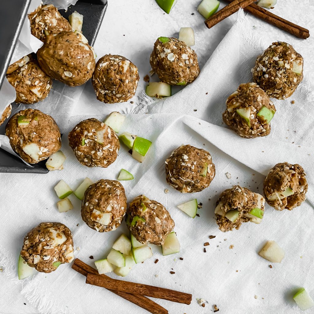 Apple peanut butter energy bites are on white linen with diced apple and cinnamon sticks scattered around.