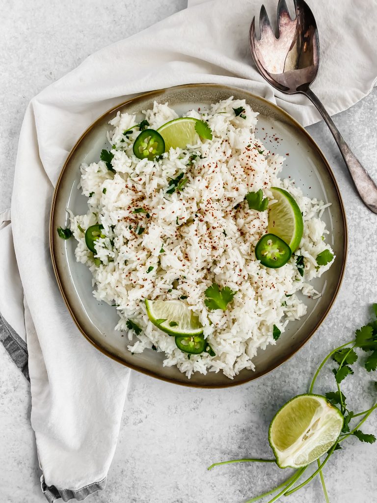 Rice on a plate garnished with seasoning, lime wedges, cilantro, and jalapenos