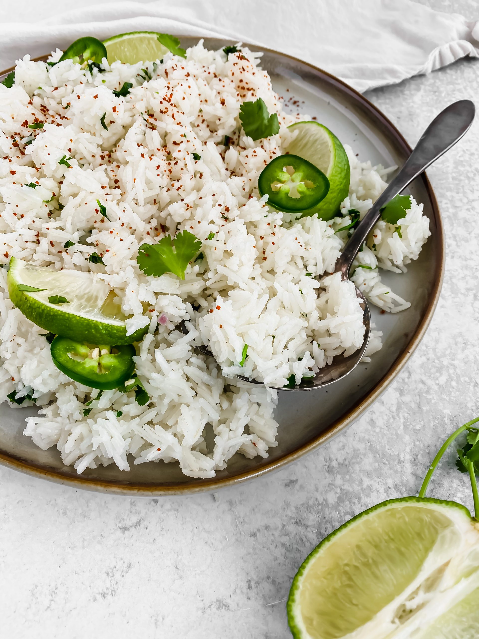 Rice garnished with a spoon, seasoning, lime wedges, cilantro, and jalapenos