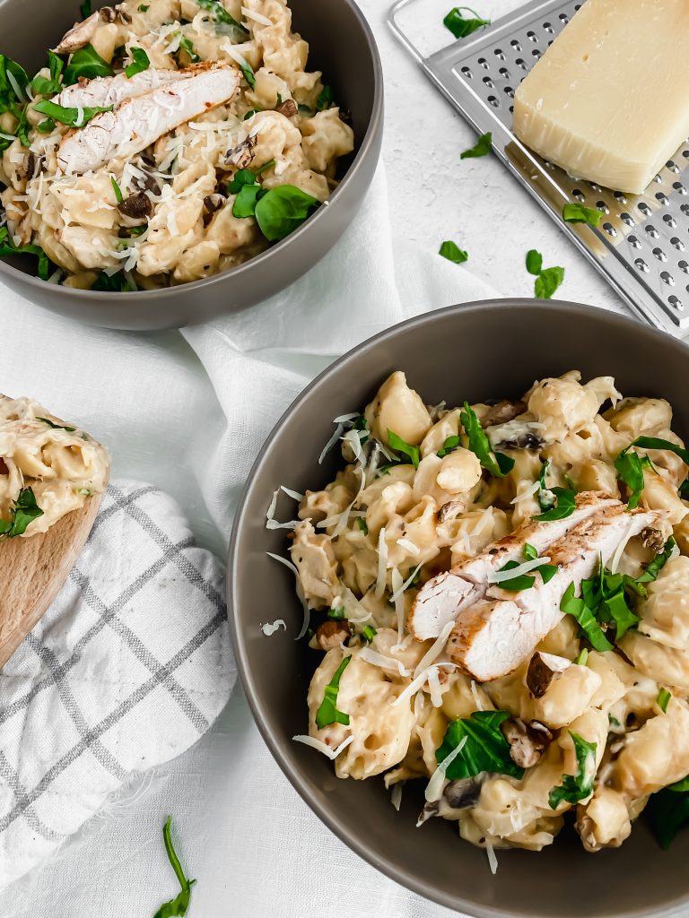 two bowls of creamy alfredo pasta garnished with sliced chicken, parmesan, and greens
