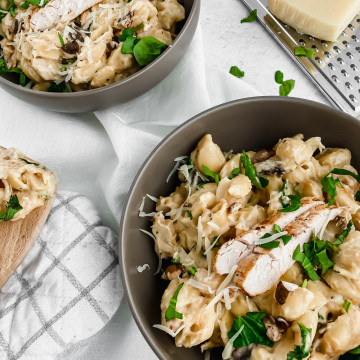 two bowls of creamy alfredo pasta garnished with sliced chicken, parmesan, and greens