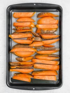 Sliced sweet potato fries fill a parchment lined baking sheet in two rows, ready to be roasted.