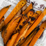 Thick sliced, roasted sweet potato fries on sheet of newspaper.