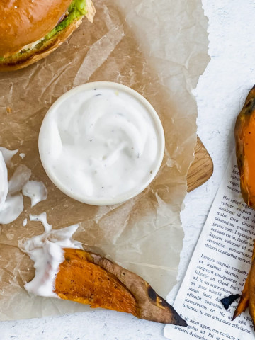 A parchment lined board is topped with two sandwiches, a bowl of ranch, and two ranch dipper sweet potato fries. There are more roasted sweet potato fries sitting to the side on a sheet of newspaper.