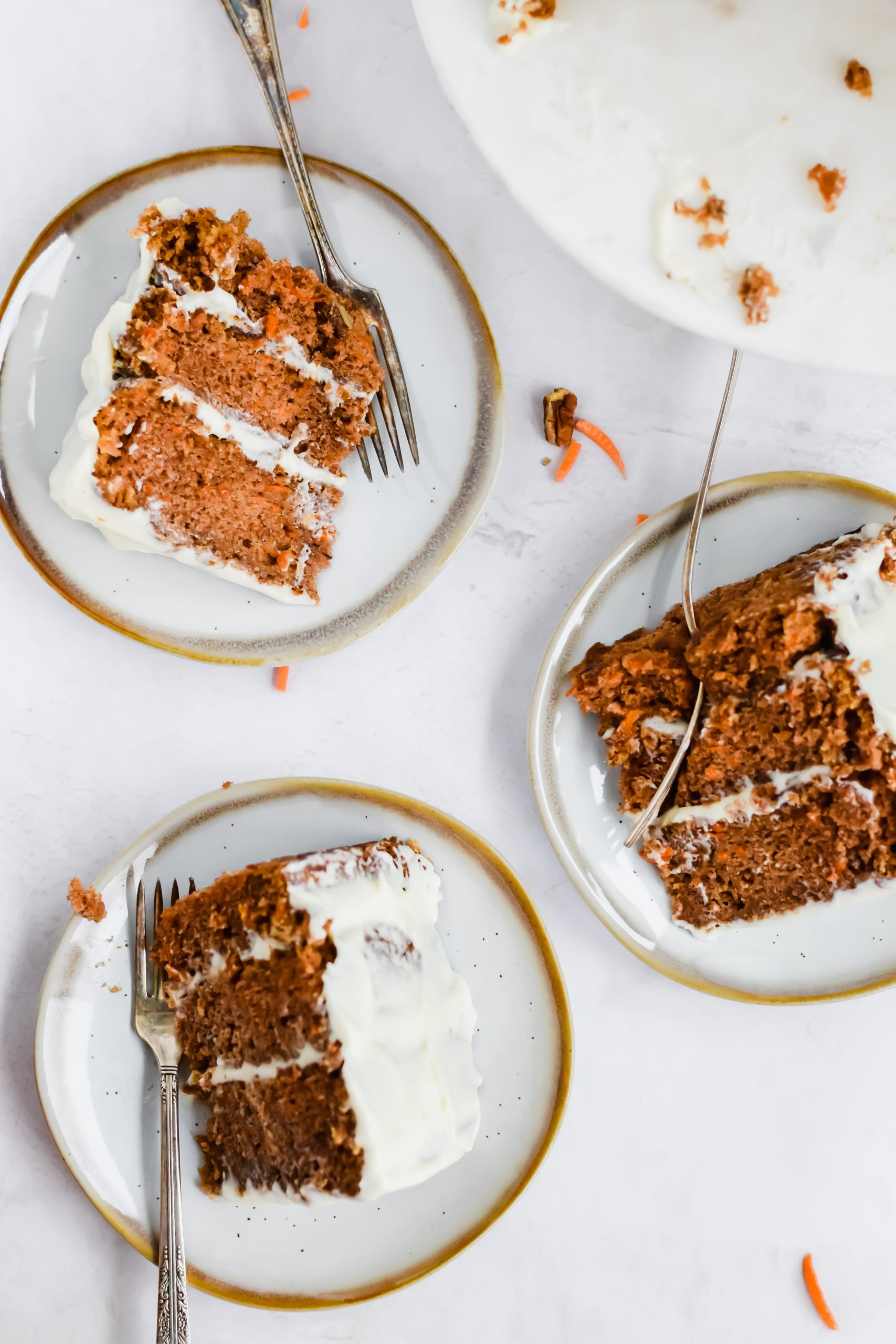 3 slices of cream cheese frosted carrot cake on a white and gold plate