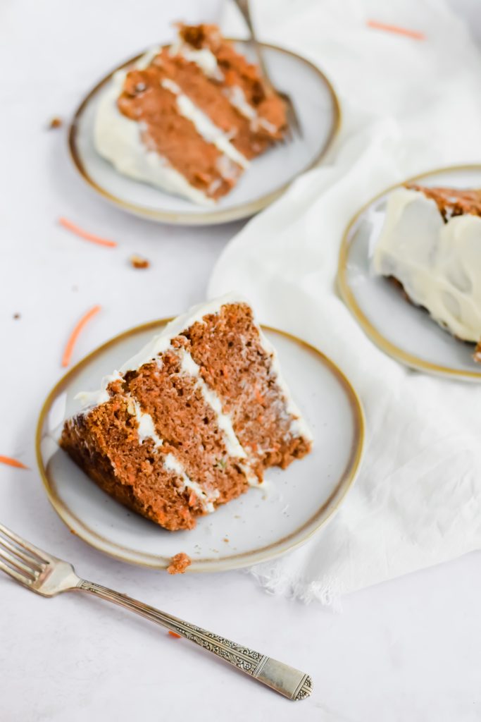 Slices of cream cheese frosted carrot cake on a white and gold plate