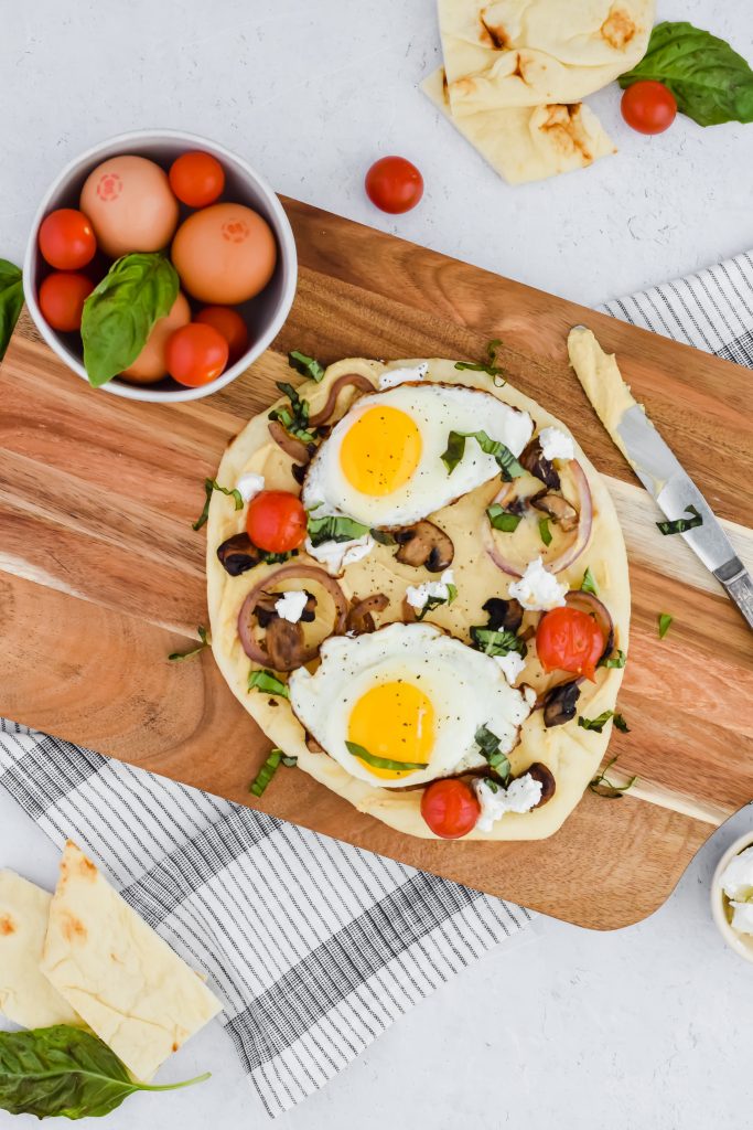 Savory Breakfast Flatbread with hummus, fried eggs, vegetables, and goat cheese