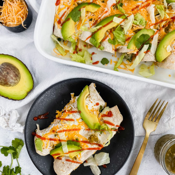 Skinny Turkey Enchiladas in a casserole dish and on a plate topped with sriracha and avocado
