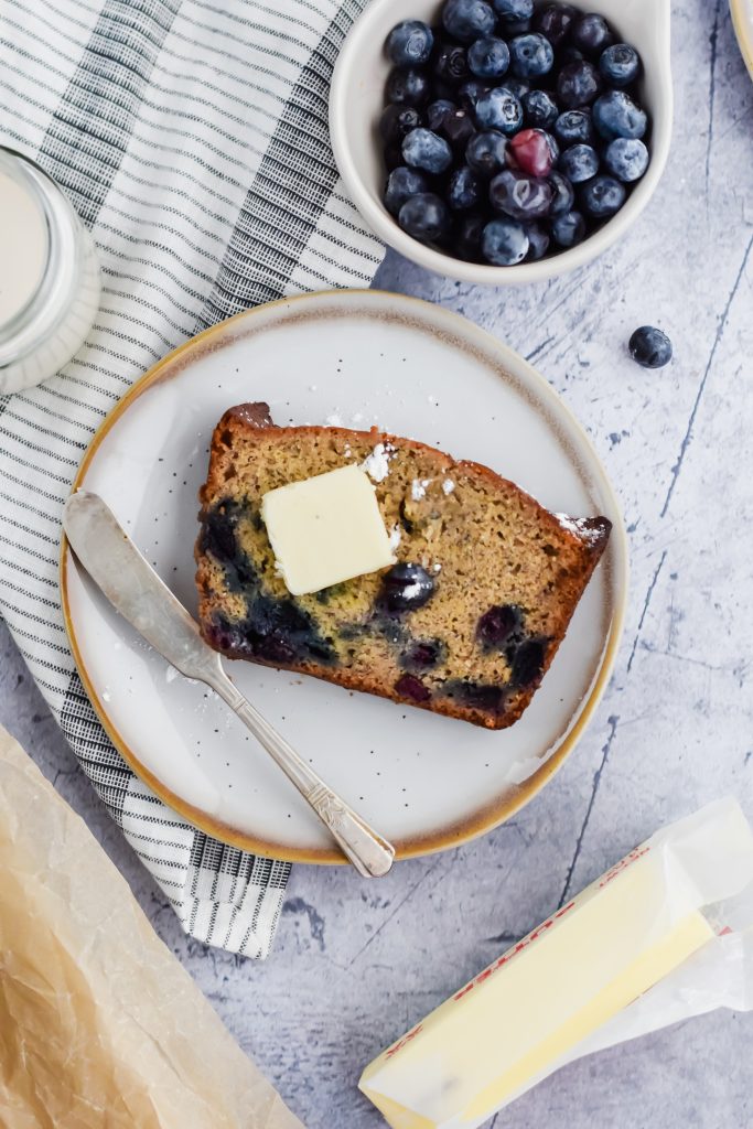 A slice of Blueberry Banana Bread with butter waiting to be spread