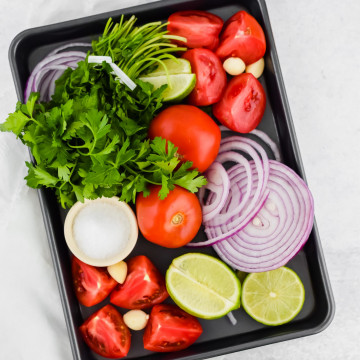 Cilantro, garlic, limes, red onion, and tomatoes on a baking sheet
