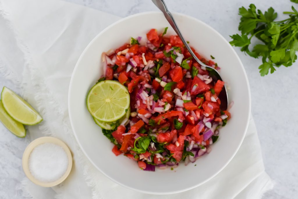 Bowl of Pico de Gallo with slices of lime and a spoon