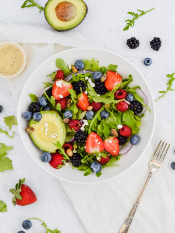 Salad bowl filled with arugula, berries, nuts, and avocado.