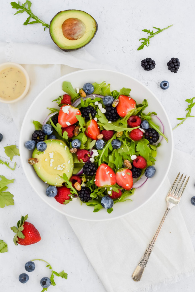 Salad bowl filled with arugula, berries, nuts, and avocado