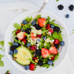 Salad in a white bowl with berries, nuts, avocado, and pale yellow dressing