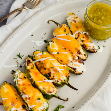 tray of air fried jalapeno poppers topped with melted cheese and salsa verde